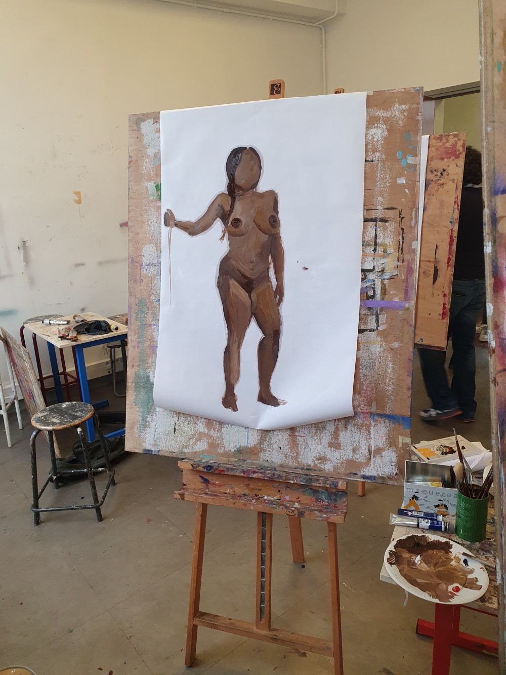 Setup during the class: a painting of a woman standing, on a easel, next
to a small table with paint tubes and brushes.