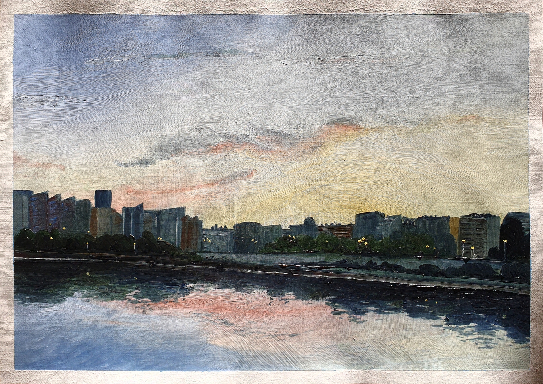 Lanscape painting of the river Seine, buildings of the city Courbevoie, and a cloud above them. The time is close to dusk, it's not dark yet but the setting sun makes the sky yellow and the clouds pink and orange. The street lights are already on, along the walkway and park that runs on the bank of the river; but the flats' windows are still dark. Oil on A3 paper.